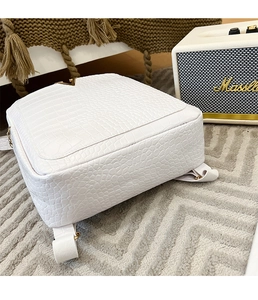 Detail of white crocodile pattern backpack with elegant gold V-shaped metal hardware