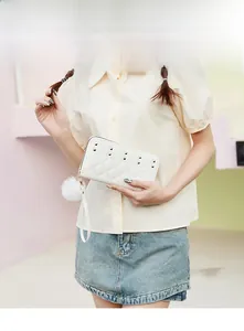Close-up of white quilted long wallet with golden studs and fluffy pompom detail