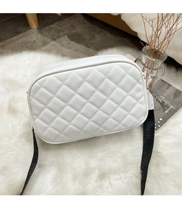 Detail of white quilted crossbody bag with embroidery and black woven strap on plush carpet