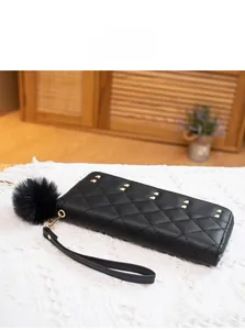 Detail view of black quilted long wallet with golden metal studs and fluffy pompom charm