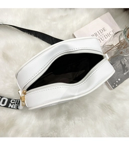 Top view of white quilted crossbody bag with black lettered strap on plush carpet