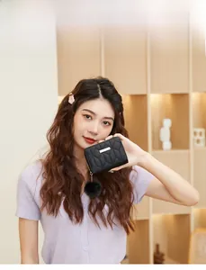 Short black quilted wallet with metal plaque and fluffy pom-pom charm held by a model
