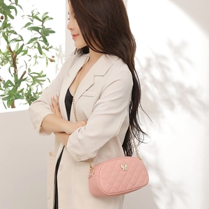 Sac bandoulière en cuir rose matelassé avec détail papillon doré porté par un mannequin