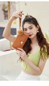 Detail of caramel glossy leather long wallet with wrist strap and plush pompom charm