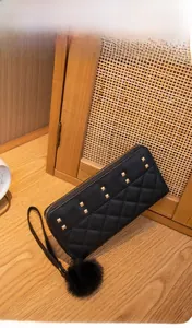 Detail of black quilted long wallet with golden studs and a fuzzy pom-pom charm