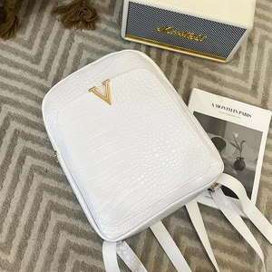 White faux-crocodile backpack with gold V-logo and zippers on a textured gray rug