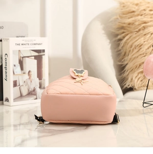 Close-up of pink quilted mini backpack with black Mickey-style metal charm on marble top
