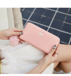 Pink faux leather long wallet for women featuring a gold butterfly and fuzzy pompom charm