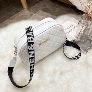 White quilted crossbody bag with embroidery and wide lettered strap on plush background