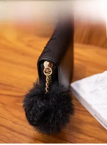 Detail of black quilted leather mini purse featuring a large fluffy pom-pom charm and gold zipper
