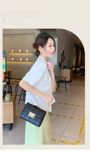 Detail of black quilted crossbody bag with gold chain strap worn by a woman in a cafe