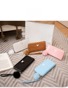 Detail of glossy patent leather wallets with metal butterfly decor and fur ball charms