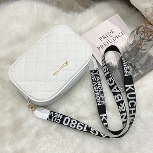 White quilted crossbody camera bag with wide jacquard strap on white faux fur background
