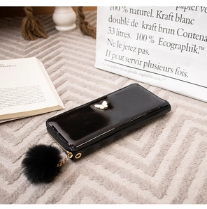 Detail of a black patent leather long wallet with butterfly ornament and fuzzy pompom
