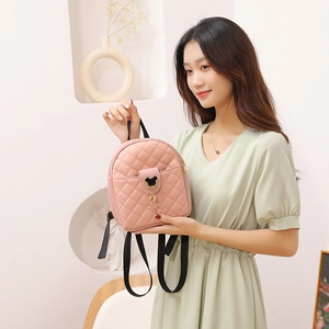 Pink quilted mini backpack with black character icon and gold accent on model