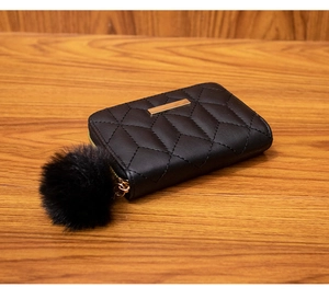 Detail of quilted leather mini wallet with gold metal bar and black fluffy pompom charm