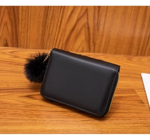 Classic black zipper wallet with a soft pom-pom keychain on a rustic wooden surface