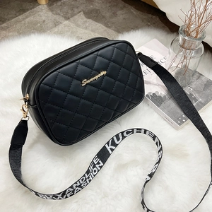 Chic black quilted crossbody bag with golden logo and patterned woven strap on plush background