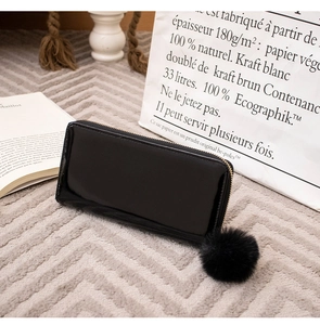 Glossy black long wallet with golden zipper and large faux fur pompom on textured rug