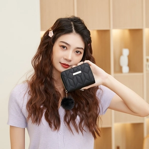 Black quilted mini purse with plush pompom and metal bar held by a female model
