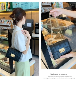 Detail of a black quilted leather crossbody bag with gold chain strap and turn-lock