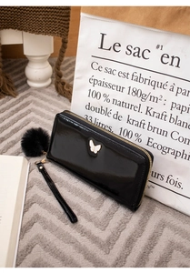 Detail of black glossy long wallet featuring a white butterfly ornament and a soft pompom
