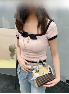 Detail of a beige and brown printed crossbody bag with scarf-wrapped handle and pink knit top