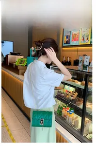 Detailed view of a green quilted chain bag with a metal lock worn by a model in a cafe
