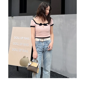 Close-up of a pink knitted top with black bow detail and checkered small square bag