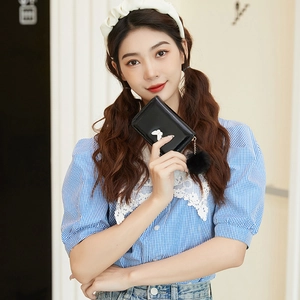 Mini black leather purse with a white bow and fluffy pompom held by a model
