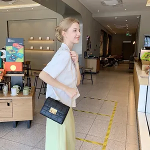 Fashionable black quilted crossbody bag with gold chain strap shown on a model in a cafe