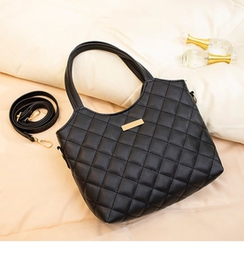 Detail of black quilted tote bag with gold metal plate and detachable shoulder strap