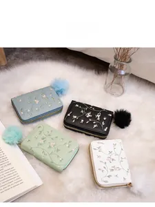 Dettaglio di mini portamonete ricamati in vari colori con ciondoli a pompon in peluche