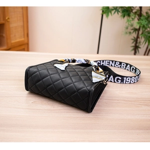 Detail of quilted black handbag with decorative silk scarf and branded wide strap