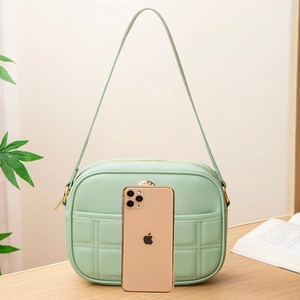 Mint green quilted crossbody bag with gold zipper and adjustable strap on a wooden desk