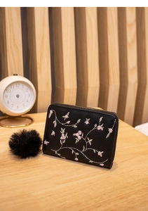 Dettaglio di portamonete nero in peluche con ricami floreali e grande ciondolo pompon