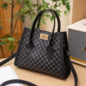 Chic women's tote bag with clover patterns and golden lock on a warm wooden desk