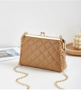 Detail of light brown quilted bag with gold metal frame and chain strap on a wooden tray