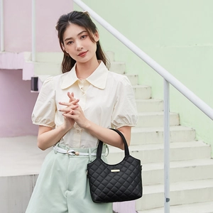Elegant black quilted tote bag with golden hardware held by a model in a stylish setting