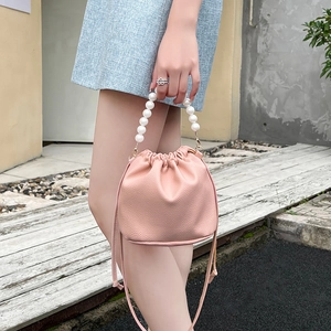 Pink drawstring bucket bag with pearl handle and leather texture shown outdoors