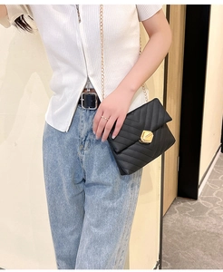 Modern V-quilted black chain crossbody bag with golden geometric clasp on a model