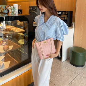 Elegant pink quilted crossbody bag with gold chain strap shown in a cafe setting