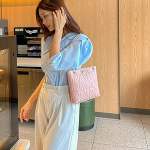 Pink quilted shoulder bag with gold chain strap worn by a model in a cafe setting