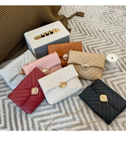 Detail view of V-quilted crossbody chain bags in multiple colors on a textured rug
