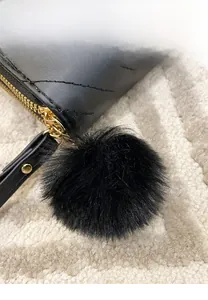 Macro detail of black quilted leather wallet with gold zipper and wool ball pendant