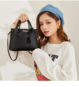 Close-up of black lychee texture leather handbag with gold metal logo and strap