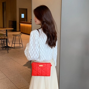 Red quilted crossbody lady bag with gold chain strap worn by model in cafe setting