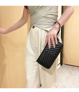 Detail of black chevron quilted long wallet with wrist strap held by hand
