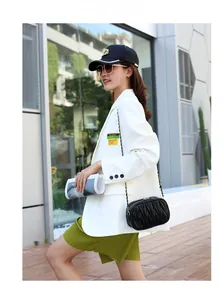 Détail d'un sac à chaîne noir matelassé avec un blazer blanc et une jupe plissée verte