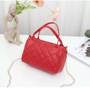 Vue détaillée d'un sac cylindrique rouge matelassé avec chaîne dorée sur table blanche